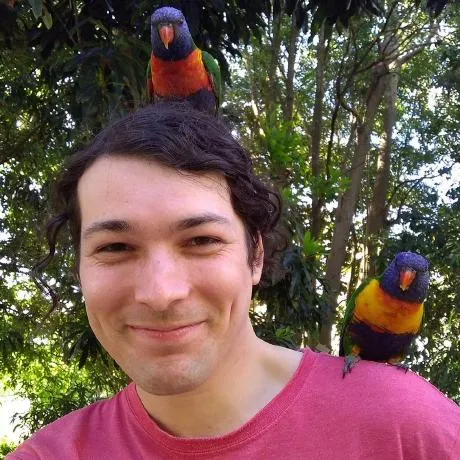 trent smiling with 2 rainbow lorikeets, 1 on shoulder, 1 on head